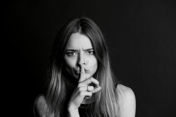The girl with long hair holds finger near the lips . The gesture of silence, secrecy, secret