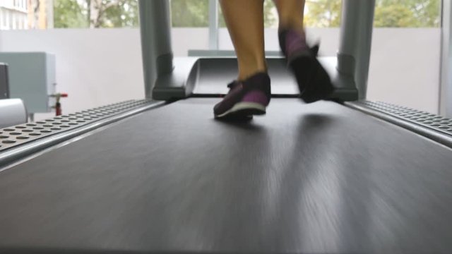 Female legs running on treadmill in gym. Young woman exercising during cardio workout. Feet of girls in sport shoes training indoor at sport club. Close up