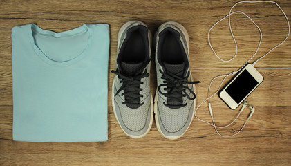 Fototapeta na wymiar Set for sports: shoes, t-shirt, mobile phone with headphones close-up on a wooden background, top view