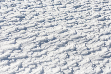 Fototapeta na wymiar Snow surface with small frozen snow waves drifted by cold wind.