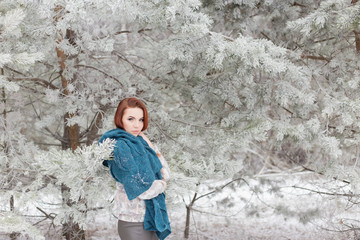 beautiful red-haired girl with a scarf on his shoulders walking in the winter forest of firs and pines stilled