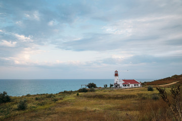 Fototapeta na wymiar Old white lighthouse on sea coast, summer landscape