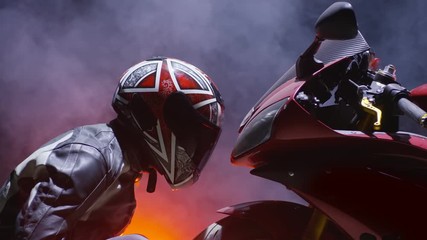 Performance of motorcyclist, looking at his motorcycle . With fire and smoke background. Shot on RED EPIC Cinema Camera in slow motion.