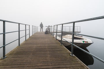 Fototapeta na wymiar Biker in the fog on the bank of lake Varese, Biandronno, Italy, at departure for the islet Virginia, important site of prehistoric finds