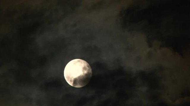 Bright, full super moon rising through cloudscape at night, time lapse.