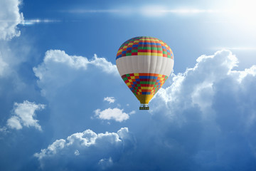Hot air balloon rises very high in blue sky above white clouds