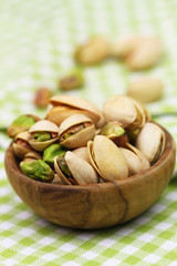 Pistachio nuts in small wooden bowl on green and white checkered cloth, closeup
