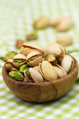 Pistachio nuts in small wooden bowl on green and white checkered cloth, closeup
