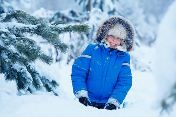 Cute little boy wearing warm clothes playing on winter forest