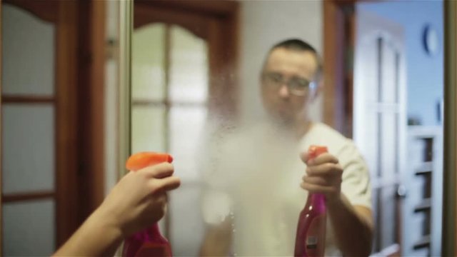 Man wetting a mirror with a cleaning solution. Slow motion.