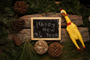 Screaming cock on wooden background with branches of fir and chalkboard as symbol of 2017 new year.