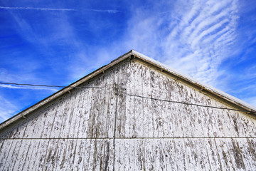 Fototapeta na wymiar A low angle of the apex of a old barn with peeling paint with blue sky in the background