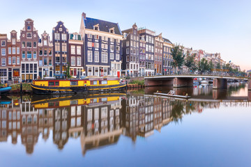 Fototapeta na wymiar Amsterdam canal Singel with typical dutch houses, bridge and houseboats during morning blue hour, Holland, Netherlands.