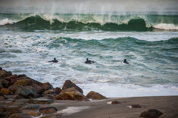 Three surfers paddling out into wind blown wave at dawn.