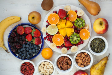 Vegan breakfast: variety of fruits, nuts and berries on the white wooden table, selective focus