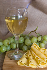still life with glass of white wine, cheese and grapes on wooden background