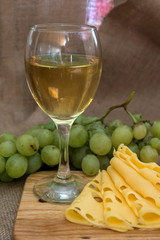 still life with glass of white wine, cheese and grapes on wooden background