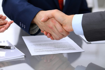 Two business man shaking hands to each other above signed contract