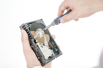 Man's hand holds open 3.5 HDD. His another hand unscrews the cover of the engine with a screwdriver. Isolated on white background.