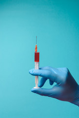 Hand in glove with syringe on blue background.