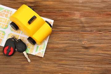 Yellow toy taxi cab, car key and map on wooden background