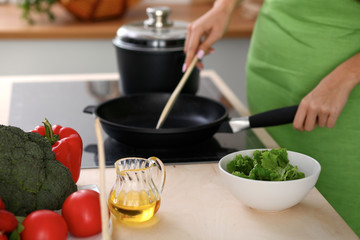 Fresh vegetables, salad and vegetable oil at the background of  woman is cooking by the stove in the kitchen