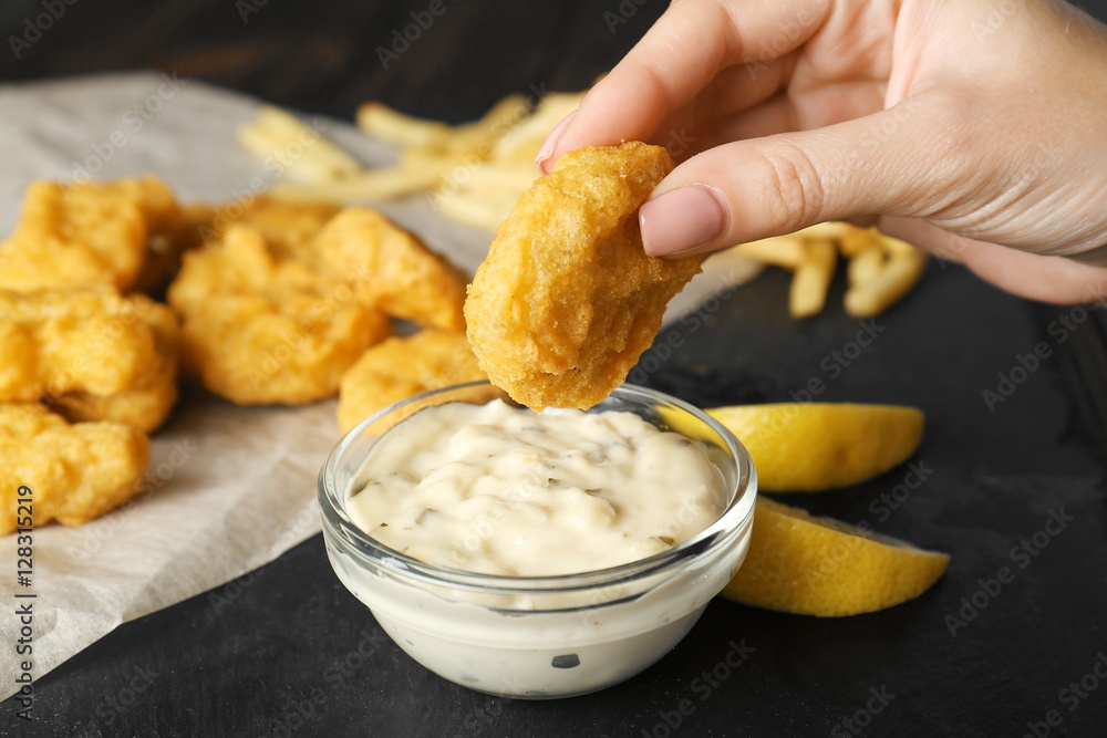 Wall mural woman holding tasty nugget and bowl with sauce on table, closeup