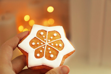 Female hand holding tasty gingerbread cookie on blurred background, close up view