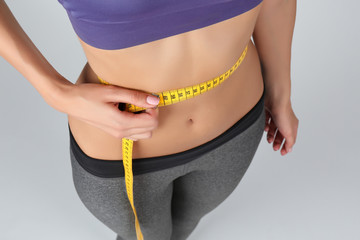 Woman measuring her waist on color background