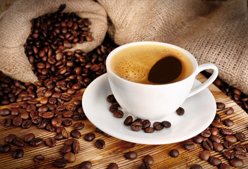 Cup of coffee with roasted beans on wooden table closeup