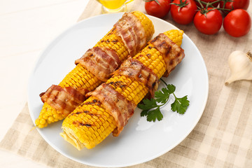 Grilled corncobs with bacon, tomatoes and parsley on plate