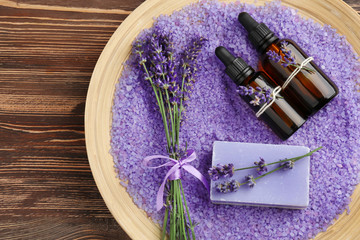 Fototapeta na wymiar Bottles of essential oil, soap and sea salt with lavender in wooden tray, top view