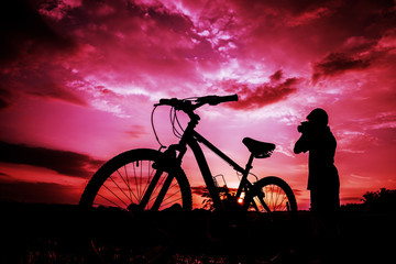 Silhouette of boy and bicycle on sunset background