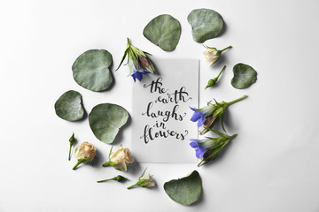 Quote "The earth laugh in flowers" written on paper with leaves and flowers on white background. Top view