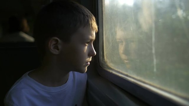 boy travelling by train looking in the window, Sun rays