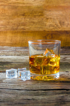 glass of whiskey with ice on a wooden table