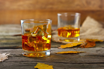 glass of whiskey with ice on a wooden table with oak leaves