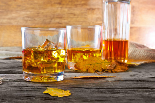 glass of whiskey with ice on a wooden table with oak leaves