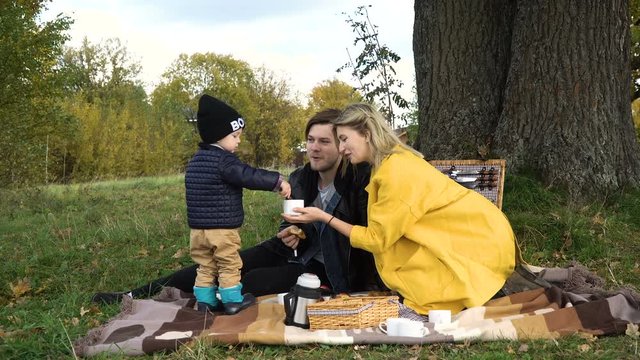 A young family with son at a picnic in the park on a sunny day.Family having picnic outdoors.Cute family picnicking in the park.Young smiling family doing a picnic on an autumns day.Family picnicking