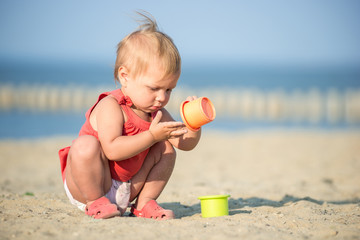 Baby playing on the sandy beach near the sea. Cute little girl in red dress with sand on tropical beach. Ocean coast.