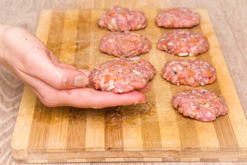 Woman's hand holding mince with grated carrots and onion in there. Cutlets creation on the wooden board in the kitchen. Healthy eating and lifestyle.