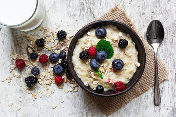 oatmeal porridge with fresh berries, glass of milk and spoon