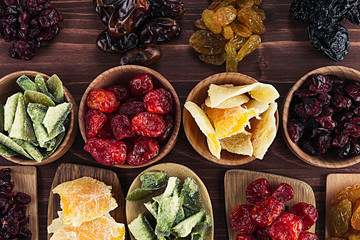 Assortment of dried fruits in spoons, bowls on brown wooden background. Decorative border of dry exotic fruit. Top view.