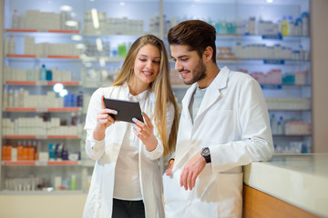 Pharmacists using digital tablet while checking medicine in pharmacy