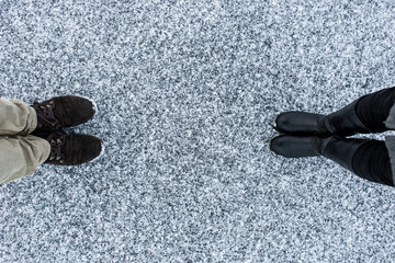 Men's and Women boots on rough snow background. Gritty snowy covered asphalt surface. Text place....