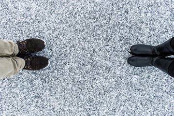 Male and Female boots standing on asphalt covered gritty snow surface. Rough snowy . Textplace....