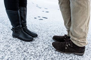 Male and Female casual boots standing on asphalt covered gritty snowy surface. Textplace. Cold Winter. Side view