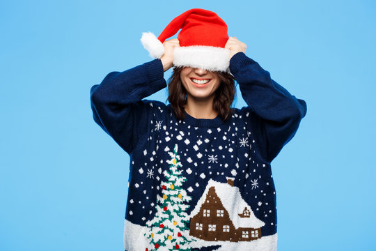 Young beautiful brunette girl in knited sweater and christmas hat smiling  over blue background.