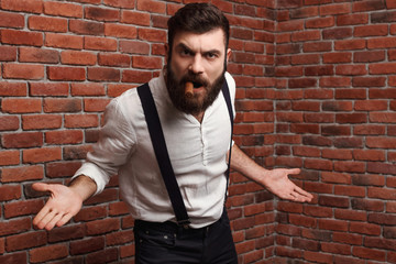 Brutal rage young handsome man smoking cigar over brick background.