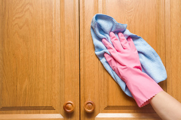 Hand in pink protective glove wiping wooden furniture with rag. Early spring cleaning or regular clean up. Maid cleans house.